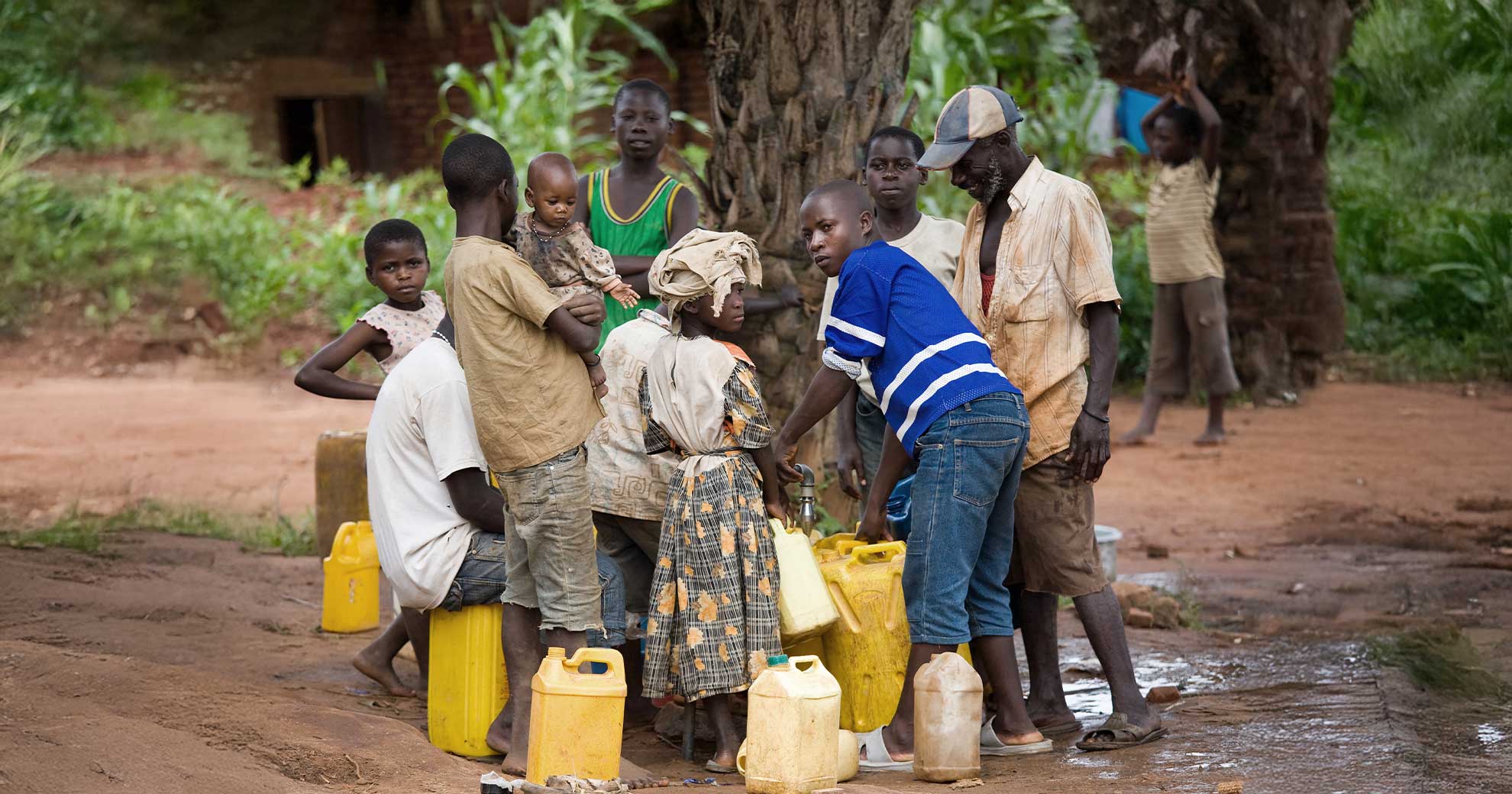 Dorfbewohnerinnen und Dorfbewohner sammeln Wasser in Kanistern an einer Quelle, Symbol fuer die globale Trinkwasserknappheit